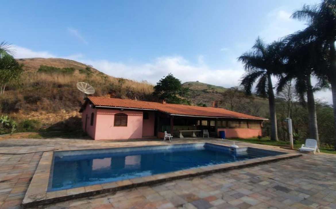 Foto, durante o dia, de piscina em frente a casa rosa com telhas de madeira.